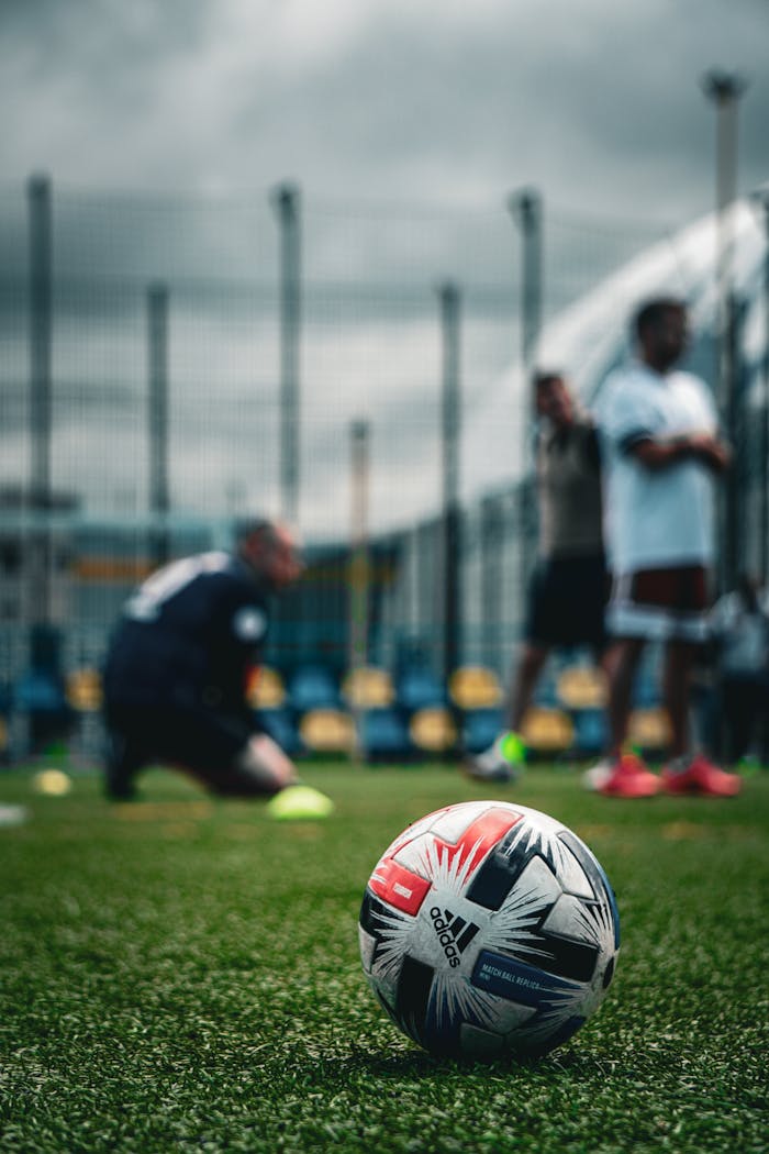 Focused soccer ball on grass field with players in the background during a cloudy day in Kyiv.