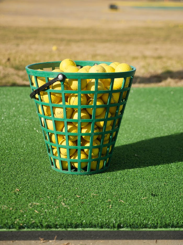 Basket filled with yellow golf balls on artificial turf outdoors.